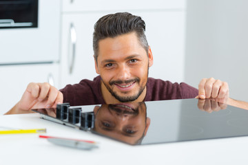 smiling man installing induction cooker in kitchen