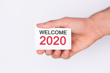 Welcome 2020 . Hand holding a white card . White background. Copy space