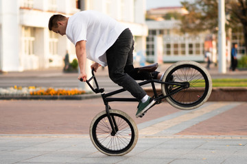 The guy on the BMX bike performs a trick on the front wheel.