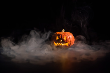 Halloween, orange pumpkin with a scary luminous face on a dark background. Thick gray smoke comes...