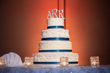 Ornate four tier wedding cake with lace fondant design on lit brown wall