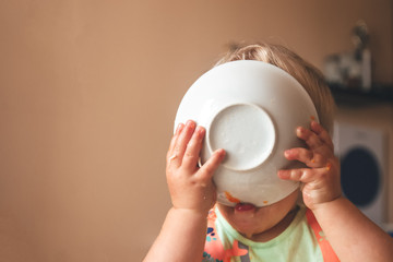 blond kid boy, very hungry eats and holds a plate with both hands, close-up with copyspace
