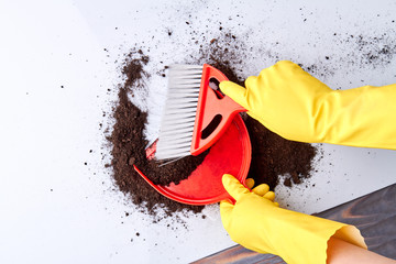 Sweeping floor with brush and dustpan. Woman in yellow gloves sweeping soil on the floor close up. Hosehold chores concept.