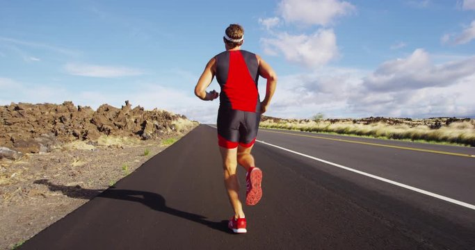 Running runner in Triathlon - Triathlete man running in triathlon suit in ironman race. Male runner exercising on Big Island Hawaii. REAL TIME STEADY TRACKING SHOT on RED Cineama Camera.