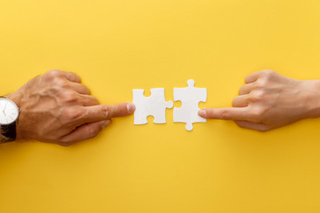 cropped view of woman and man matching pieces of white jigsaw puzzle on yellow background