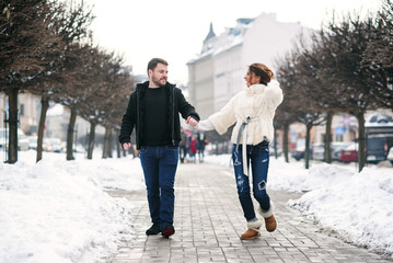 Fototapeta na wymiar Beautiful happy girl and her handsome boyfriend walking together on the winter snowy street. New Year and Christmas concept.