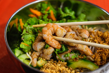 Asian food, wok, spicy seafood, shrimp and vegetables close-up on rice noodles with chopsticks closeup in the bowl