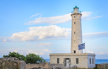 Obraz premium A lighthouse with a greek flag against a cloudy blue sky in Gytheio Greece