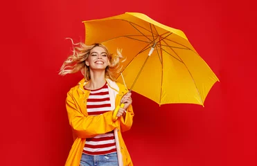Fotobehang young happy emotional cheerful girl laughing and jumping with yellow umbrella   on colored red background. © JenkoAtaman