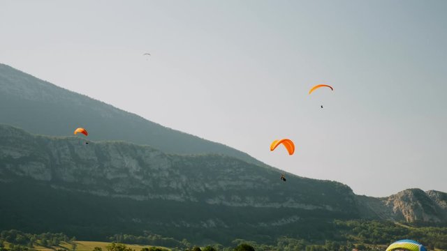Orange paraplanes flying above Alps mountains. Paraglider flying against blue sky and mountains in Alps. Paragliding lessons