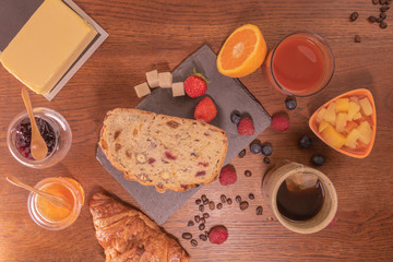 Petit déjeuner varié avec pain aux fruits secs et céréales jus d'orange frais miel et confiture de fraise, beurre thé et fruits rouges et salade de fruits grains de café et croissant