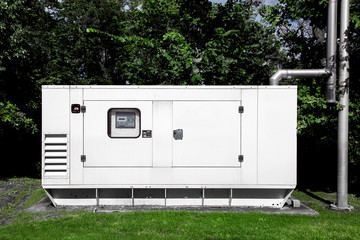 backup diesel electric power emergency generator mounted on a green lawn with green trees and a...