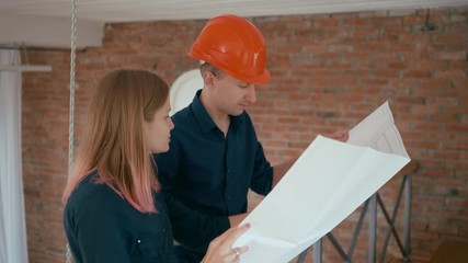 Young Female Architect Discusses Project Drawing with Contractor or Constructor in Orange Hard Hat indoors in Red Brick Building. 4K Medium Static Shot