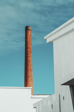 A vertical shot of a red brick funnel behind building roofs and white walls with the lightning-rod on the top and the sky in the background, Lisbon, Portugal