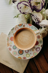 cup of coffee, notebook and white flowers on a wooden table
