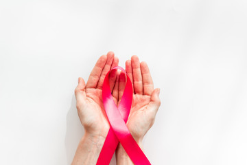 Pink ribbon in hands as symbol of breast cancer awareness on white background top view copy space