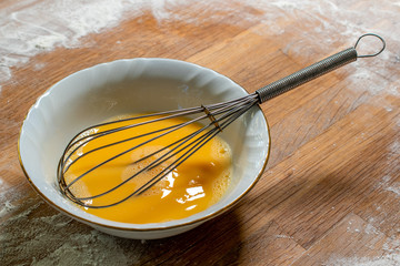 Mixed egg in a porcelain bowl with a steel whisk