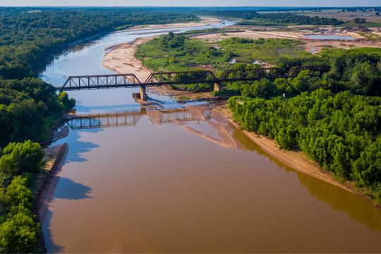 Aerial photo of Train trestle crossing muddy river that winds into the landscape on the Texas and Oklahoma border | Train tracks crossing river