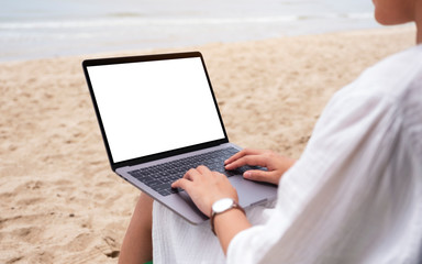 Mockup image of a woman using and typing on laptop computer with blank desktop screen while sitting on a beach chair