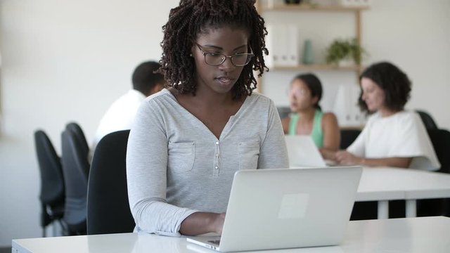 Focused African American woman using laptop at office. Front view of concentrated employee with dreadlocks typing on laptop. Technology concept