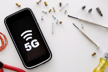 A smartphone displaying 5G symbol with tools and screws on table. Concept for upgrading to 5G, 5G...