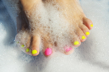 Female legs with bright yellow and pink varnish in a foam bath. In bright sunshine. The shadows...