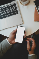 Top view of young businessman holding blank screen smartphone while working on his project