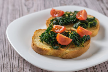 Cherry tomatoes and roasted greens on slices of bread on a wooden table.