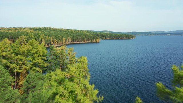 Aerial panoramic view of Turgoyak national park with beautiful pure water of lake and relict forest with pines, birches; autumn sunny evening with colorful foliage of deciduous trees; famous landmark