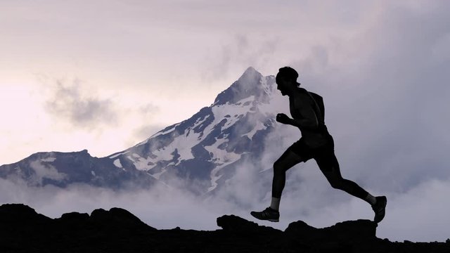 CINEMAGRAPH - seamless loop video. Running man athlete silhouette trail running in mountain summit background clouds. Man on run training outdoors active fit lifestyle. Looping Motion photo image.