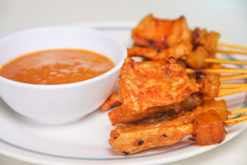 Pork Satay barbecue and white cup with peanut sweet sauce on plate thai food background