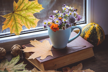 blue cup with flowers on the windowsill and autumn leaves.