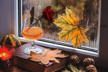 red rose in a glass on a windowsill and autumn leaves.