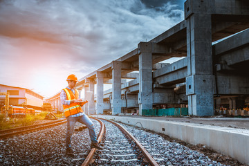 A engineer under inspection and checking construction process railway work on rail train station by Blueprint  on hand . Engineer wearing safety uniform and safety helmet in work.