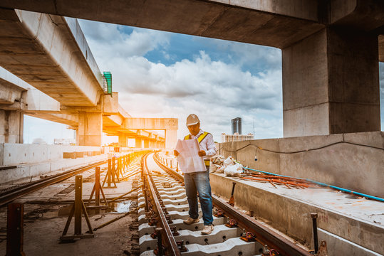 A Engineer Under Inspection And Checking Construction Process Railway Work On Rail Train Station By Blueprint  On Hand . Engineer Wearing Safety Uniform And Safety Helmet In Work.