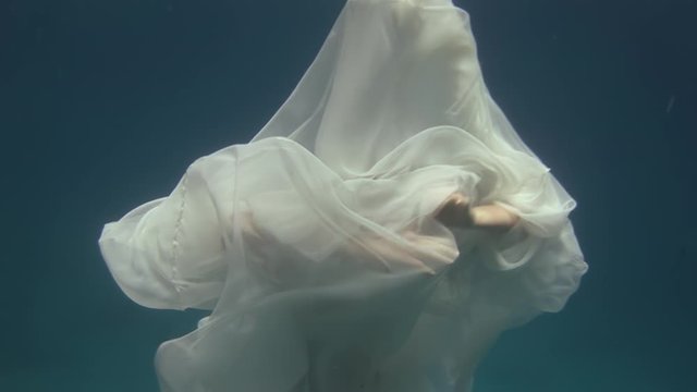 Young woman underwater model in white cloth on background of blue water. Concept of creativity and art of creating images.