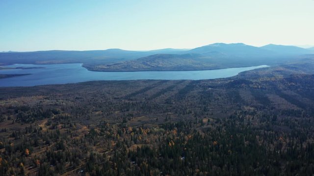 Aerial drone view of Zuratcul lake in autumn surrounded by Ural mountains, hills, mixed forest with green pines and yellow birchs; colorful trees on coasts; fragile ecosystem and anthropogenic impact