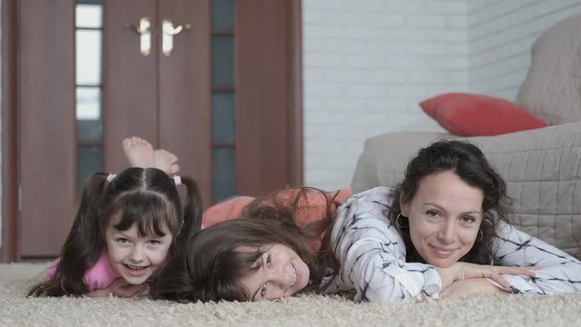 Mother with children are lying on the floor. Happy little girls are having fun with mom.