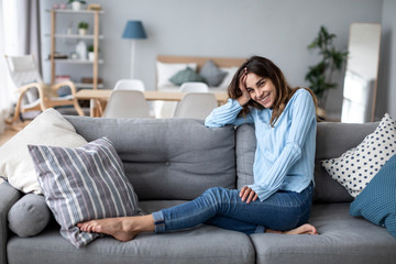 Obraz premium Happy casual beautiful woman sitting on a sofa at home.