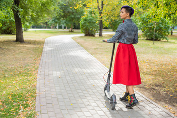 A young woman with purple hair rides an electric scooter in a park. A stylish girl with a shaved...