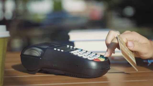 Close-up of woman rotating credit card in hands applying on pos reader for checkout and wireless money transaction. Credit card payment. Outdoor view.