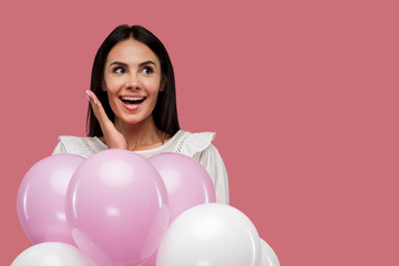 excited woman holding balloons isolated on pink