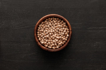 top view of brown bowl with raw chickpea on dark wooden surface with copy space