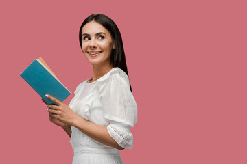 happy young woman in dress holding book isolated on pink