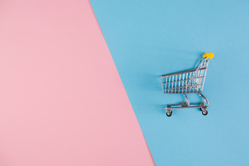 Shopaholic. Buyer. Shopping concept. Close-up. An isolated trolley and shopping basket on a pink and blue background bisected. Copy space.