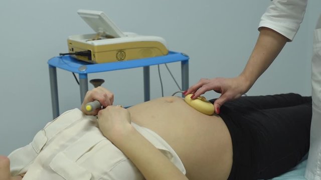 A gynecologist examines a pregnant woman. Fetal doppler heart auscultation. Patient at doctor office. Assessment of heartbeat and control of all fetal cardiac activity. Concern about the health.