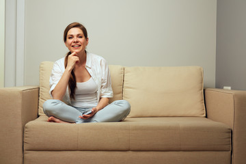 Fototapeta na wymiar Smiling woman sitting on sofa at home using smartphone.