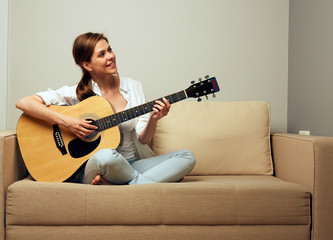 woman playing on guitar sitting on sofa.