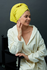 Smiling woman in bathrobe and towel on head has photo shoot in photo studio.