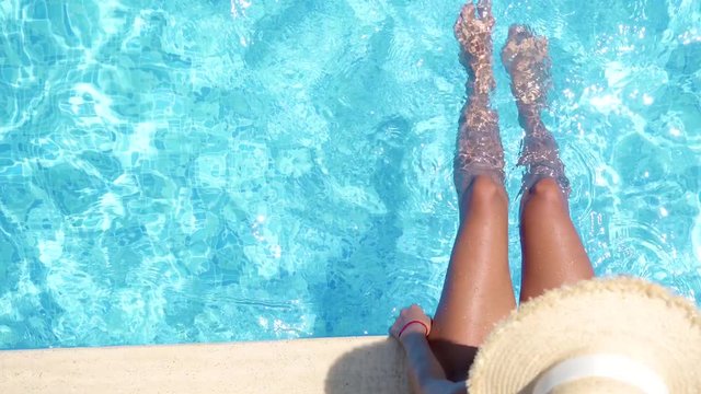 Girl in bikini relaxing in swimming pool in sunny day. Beautiful sexy girl in summer pool splashing water with feet. Top view of female beautiful legs in water. 4K